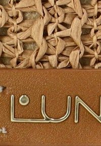 Textura de fibra natural trenzada en marrón claro con un acento de cuero suave en tono arena. Letras en tono dorado que dicen "LUN."