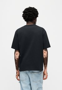 Μαύρο βαμβακερό μπλουζάκι με χαλαρή γραμμή, στρογγυλή λαιμόκοψη και κοντά μανίκια. Φορεμένο με ανοιχτό μπλε τζιν παντελόνι cargo, που αναδεικνύει μοναδικά μοτίβα στα μανίκια.