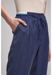 Pantaloni blu navy fatti di tessuto testurizzato; presentano un elastico in vita con una banda orizzontale azzurro e bianco e tasche laterali.