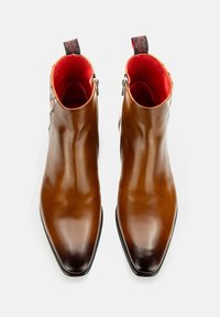 Braune Leder-Ankle-Boots mit spitzer Zehenform, glatter Textur und kontrastierendem roten Innenfutter, ausgestattet mit seitlichen Reißverschlüssen und schwarzen Ziehschlaufen.