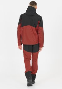 Vattentät jacka och byxor i röd och svart. Jackan har en huva, en kombinerad färgblockdesign och slitstarkt tyg. Byxorna har mjuka delar i softshell.