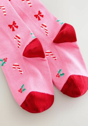 Rosa Socken mit roten Zehen- und Fersenakzenten, verziert mit Zuckerstangen und Schleifen in Grün und Rot. Hergestellt aus einem weichen, dehnbaren Stoff.