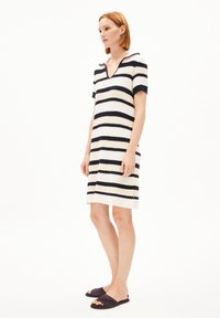 Randig stickad klänning i vitt och marinblått, korta ärmar, V-ringning, knälång med sidslitsar; bärs med svarta sandaler.