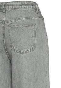 A szürke farmernadrág hátsó zsebében enyhén átlós varrás található, magasított derékrésszel és puha, texturált anyagból készült.