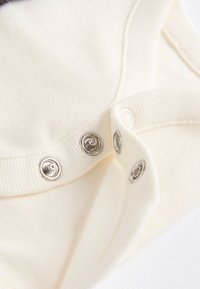 Cream-colored cotton bodysuit with silver snap fasteners at the base and soft ribbed neck and arm edges. Smooth texture, seamless design.