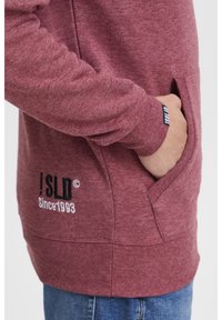 Bordeaux hoodie van een gestructureerde stof, met een kangoeroezak, geribbelde manchetten en een logo met de tekst "!SLD Sinds 1993" in contrasterend wit.