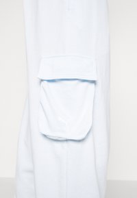 Jogging en bleu clair fabriqué en tissu doux avec une poche à rabat et un logo Puma blanc sur le côté. Coupe simple et décontractée avec une texture lisse.