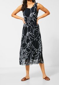 Černé maxi šaty bez rukávů s bílým botanickým liniovým uměním. Mají přiléhavý pas a splývavou sukni, vyrobené z lehkého materiálu. Nosit ploché sandály.