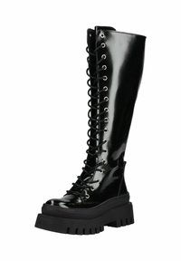 Botín de combate alto de charol negro brillante con suela gruesa de tacos y cordones negros pasados por ojales de metal.