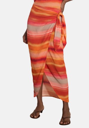 Femme portant une jupe portefeuille rayée orange vif, rose et beige avec un lien sur le côté, associée à des sandales marron à talons.