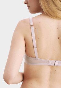 Soutien-gorge rose clair avec bretelles réglables. Il présente un tissu lisse et une fermeture à crochets. Bande en mesh respirante pour le confort.