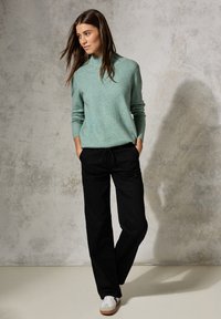 Mintgrön stickad tröja med ribbade ärmslut, i kombination med svarta vida byxor med dragsko och vita skor med beige detaljer.