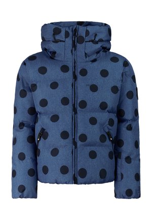 Kind draagt blauwe ski-jas met stippen, zwarte skibroek, zwarte laarzen, blauwe muts en zwarte skibril, staand met één hand in de zak.