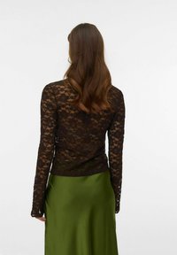 Czarna koronkowa bluzka z długim rękawem o kwiatowym wzorze, nałożona na zieloną satynową spódnicę, prezentująca dopasowany krój i przezroczystą teksturę.