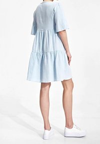 Hellblaues, gestuftes Kleid aus strukturiertem Stoff mit kurzen Ärmeln. A-Linie, knielang, kombiniert mit weißen Sneakers.