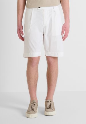 Witte katoenen shorts hebben een relaxte pasvorm, omgeslagen zoom en centrale plooien, gecombineerd met beige suède sneakers.