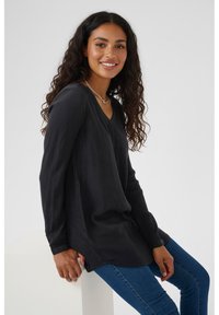 Long-sleeve black shirt with a V-neck, made of textured fabric, featuring a relaxed fit and side slits, paired with blue jeans.