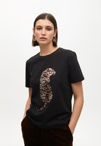 T-shirt nera con design di una tigre realizzato in paillettes lucide e multicolori. Maniche corte, colletto a girocollo, vestibilità comoda.