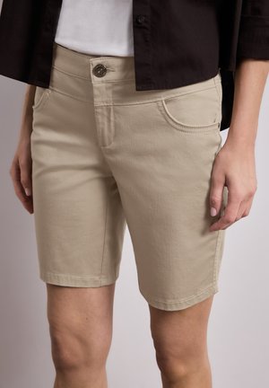 Beige knielange shorts met voorzakken, gedragen met een wit overhemd en een zwart open jack, getoond van taille tot knieën.