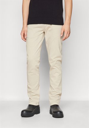 Beige cotton chinos with a slim fit, featuring side pockets and a smooth texture, paired with black chunky-soled boots.