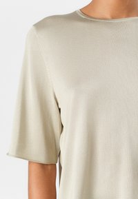 Light beige short-sleeve top made from smooth, ribbed fabric. Features a round neckline and subtle stitching details along the sleeves.