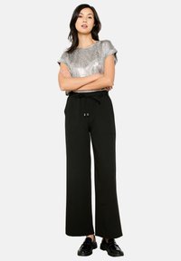 Metalni srebrnactually krojeni top s kratkimi rokavi z diskrétno vzorcem, v kombinaciji z ohlapnimi črnimi hlačami, ki imajo elastični pas in stranske žepke.