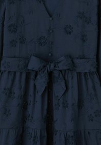 Robe bleu marine ornée de broderies florales, avec un décolleté en V, des boutons de fermeture et une ceinture nouée à la taille avec une texture brodée.