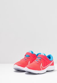 Czerwone siateczkowe sneakersy z niebieskimi akcentami, wyposażone w rzep i sznurówki, z białą podeszwą oraz detalem logo z boku.