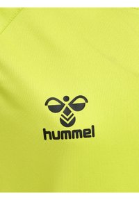 Lys gul sportstøj med en glat tekstur, der har et sort Hummel-logo med et karakteristiskt design og skrifttype.