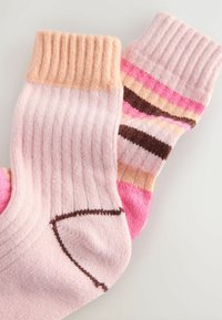 Knit socks in pink hues. One sock has a ribbed cuff with solid pink, the other features stripes in pink and brown. Textured finish.