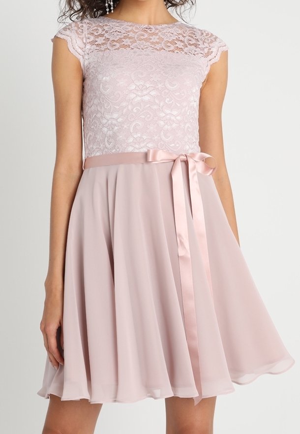 Robe sans manches rose pâle avec corsage en dentelle, encolure transparente, ruban de satin à la taille noué en nœud et jupe fluide longueur genou.