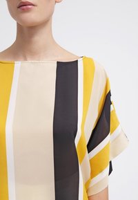 Luźna bluzka z ukośnymi paskami w kolorze żółtym, czarnym i kremowym. Miękka, lekka tkanina z szerokim dekoltem i krótkimi rękawami.