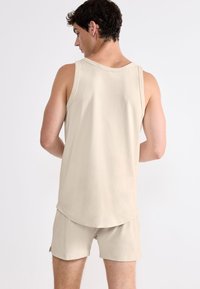 Beżowy top na ramiączkach o luźnym kroju i okrągłym dekolcie, zestawiony z dopasowanymi szortami, wykonany z miękkiego materiału i z minimalnymi detalami szwów.