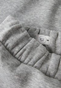 Close-up van grijze elastische tailleband met verstelbare witte knoop en zachte ribbelstoftextuur.