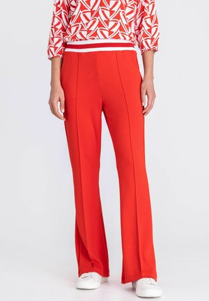 Femme portant un pantalon taille haute rouge vif avec des coutures à l'avant, associé à un haut à motif rouge et blanc et des baskets blanches.