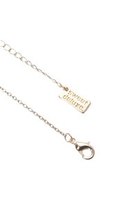 Guld färgad kedja halsband med en rektangulär tagg inskriven "sweet deluxe" och en metall klämma, med en slät yta.