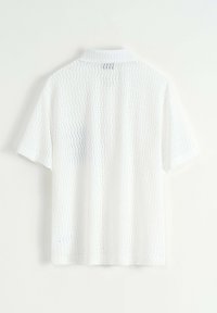 Chemise blanche à manches courtes en tissu texturé et tissé. Design avec col et un motif subtil, avec une petite étiquette au dos du col.