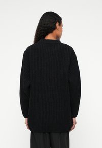 Musthave mustrida, musta tekstuuriga kudum, millel on lahtine lõike, pikad varrukad ja soonikäär. Seljaview näitab ümarat äärealust ja peent detaili.