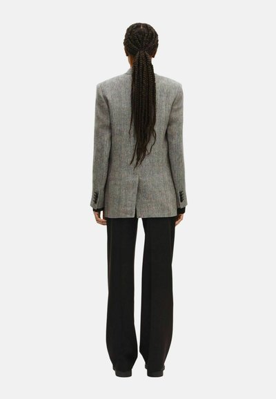 Grau gestreifter Blazer mit strukturierten Schultern und schwarzen Hosen, von hinten gezeigt. Lange, geflochtene Haare sichtbar.
