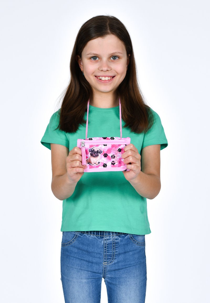 Portafoglio di tessuto rosa con stampa di carlino, motivi neri a forma di zampa e una cerniera. Tenuto da un bambino in una maglietta verde, con una tracolla per trasportarlo.