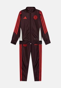 Tuta Adidas di un elegante bordeaux scuro con strisce rosse. Caratterizzata da una giacca con zip e pantaloni abbinati. Realizzata in tessuto liscio con un design sportivo.