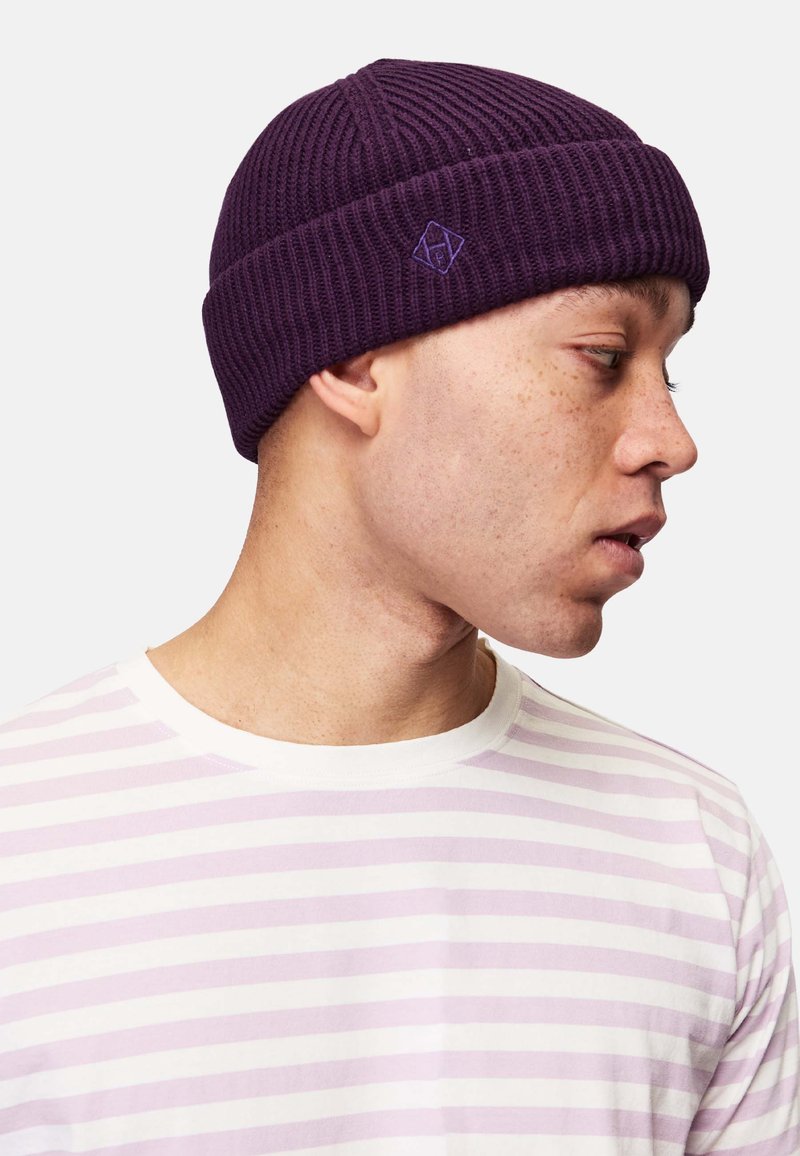 Violetti ribattu neulepipo, jossa on käännetty reunus ja pieni logo-ommel. Yhdistetty vaaleanraidalliseen paitaan, jossa on violetteja ja valkoisia raitoja.