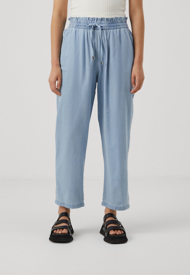 Light blue relaxed-fit pants with an elastic waistband and drawstring, featuring a smooth texture and cropped length. Paired with black sandals.