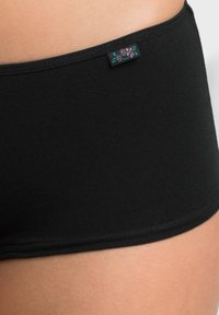 Boxer in cotone nero con una texture liscia, caratterizzati da un accento con motivo floreale vicino all'elastico in vita. La vista ravvicinata sottolinea l'elasticità del tessuto.