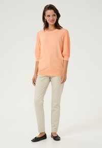 Pull en pêche avec des manches bouffantes texturées, associé à un pantalon slim beige clair et des ballerines noires. Design simple et élégant.