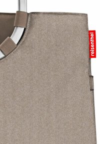 Nahaufnahme einer beigefarbenen Stofftasche mit Fischgrätmuster, die an einem grauen Metallrahmen befestigt ist, sowie einem roten Reisenthel-Tag.