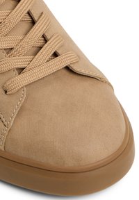 Sneaker marrone chiaro realizzato in un materiale simile alla pelle scamosciata, con punta tonda e lacci testurizzati. Suola in gomma con un leggero motivo a battistrada.