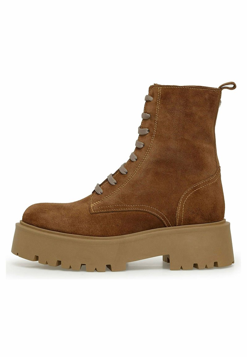 Brune ruskindsstøvle med rund tå, grå snørebånd og en kraftig, tekstureret beige sål. Har dekorativ syning langs siden.