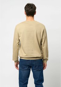 Beige katoenen sweatshirt met lange mouwen, een ronde hals en geribbelde manchetten, gecombineerd met donkerblauwe denim jeans met achterzakken.