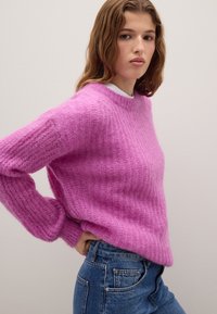 Maglione rosa a maglia con un motivo testurizzato, scollo rotondo e maniche lunghe, abbinato a jeans a vita alta blu scuro.